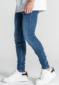 Skinny blue denim jeans with a distressed texture, paired with white sneakers featuring a black heel accent.
