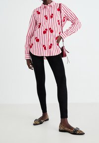 Chemise à manches longues rayée avec broderie florale rouge sur fond blanc, associée à un pantalon noir slim et des ballerines imprimé léopard.