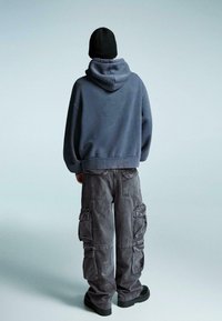 Tmavě šedá oversized mikina s texturovanou tkaninou. V kombinaci s volnými cargo kalhotami s několika postranními kapsami a uvolněným střihem. Černá čepice.