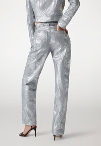 Completo due pezzi in satin silvero con un motivo a foglia in rilievo. La giacca corta e i pantaloni dritti hanno una finitura lucida e tasche.