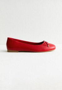 Ballerine in pelle rossa con punta rotonda e un piccolo fiocco decorativo. Presenta una superficie strutturata e un tacco basso di colore chiaro.