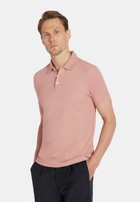 Jasnoróżowa, krótko rękawowa koszulka polo z klasycznym kołnierzykiem, trzema guzikami z przodu oraz subtelnym detalem logo na klatce piersiowej. Miękka bawełniana tekstura.