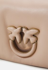 Borsa in pelle beige chiaro con manico curvo e due dettagli a forma di farfalla, contornati in oro, e una superficie texturizzata.
