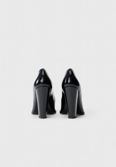 Cizme cu toc înalt din piele lacuită neagră, cu o textură netedă, vârfuri ascuțite și tocuri late, care evidențiază un design elegant și modern.