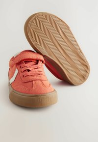 Buty na rzep w jasnym koralowym kolorze, wykonane z miękkiego materiału z gumową podeszwą. Posiadają białe akcenty i teksturowany wzór w zygzaki na podeszwie.