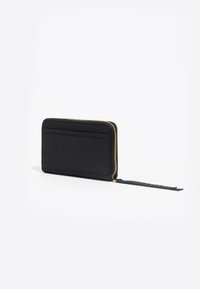 Portafoglio nero con zip, dalla superficie testurizzata, dotato di scomparti per carte da un lato e un elegante dettaglio con nappina. Finiture in oro visibili.