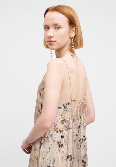 Robe transparente beige à imprimé floral avec fines bretelles, dos ouvert noué avec un ruban, présentant de délicats motifs floraux et une texture légère.