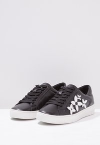 Black leather sneakers with white floral accents, lace-up design, cushioned sole, and smooth texture. White rubber outsole for grip.