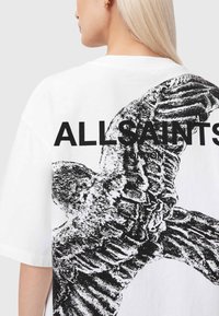 Λευκό υπερμεγέθες μπλουζάκι με μεγάλο μαύρο γραφικό σχέδιο ενός πουλιού και το κείμενο "ALLSAINTS" στην πλάτη. Μαλακή υφή από βαμβάκι.