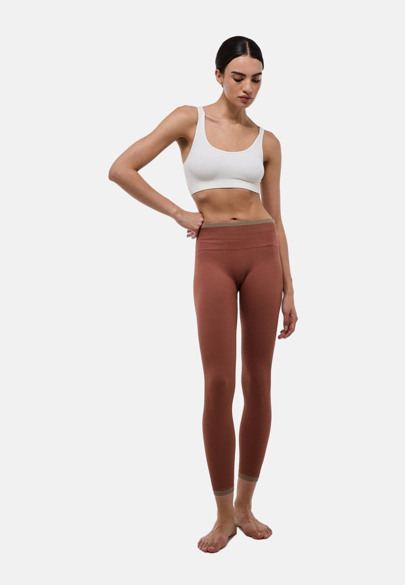 Leggings marron à côtes avec une taille large et douce, et des accents marron clair au niveau des chevilles, associés à un top court à côtes blanc.