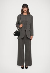 Abito a righe sottili in grigio con blazer doppiopetto, pantaloni a gamba larga e una borsa nera a tracolla. Presenta bottoni lucidi e una vestibilità su misura.