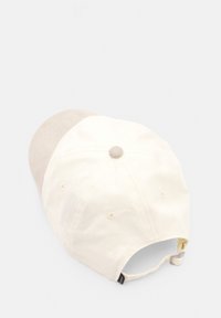 Cotton baseball cap with a cream body and a beige suede brim, featuring ventilation eyelets and an adjustable strap at the back.
