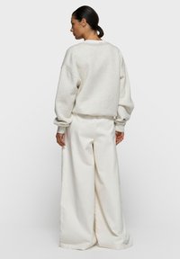 Sweat-shirt gris clair, surdimensionné, avec épaules tombantes et manches longues, assorti à un pantalon blanc cassé à jambes larges, le tout confectionné dans des matériaux doux.