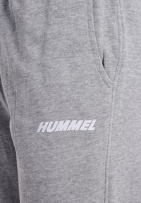 Grå joggingbukser lavet af bomuldsblandet stof med sidelomme og hvidt "HUMMEL" logo langs benet. Tekstureret, afslappet design.