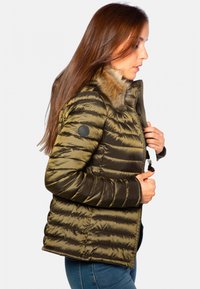 Doudoune vert olive avec coutures horizontales, col en fourrure, patch logo noir sur la manche et fermeture zippée. Texture lisse et brillante.