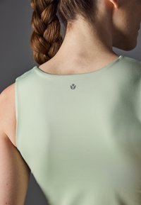 Top deportivo sin mangas de color verde menta con una textura suave, escote redondeado y detalle del logo en la parte posterior cerca del cuello.