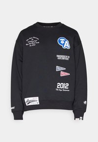 Sweat-shirt noir col rond avec logos blancs et bleus, texte incluant "2012 The Aape Universe" et petits patchs graphiques sur le devant et les manches.