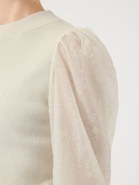 Cream ribbed knit top with sheer, embroidered puff sleeves featuring floral patterns and a soft texture. Rounded neckline.