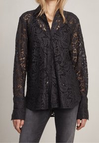 Camicia nera in pizzo con motivo floreale, maniche lunghe e design con bottoni. Il tessuto è semi-trasparente con una finitura testurizzata.