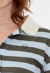 Polo rayé avec des rayures bleu clair et vert foncé, un col blanc et un détail de logo positionné sur la poitrine.