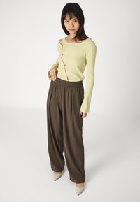 Lys grønn ribbet langermet topp med detaljknapp og off-shoulder-design, sammen med brune vide bukser og beige spisse hæler.
