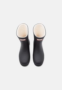 Black rubber rain boots with a soft cream lining, featuring a rounded toe and a small logo patch near the top edge.
