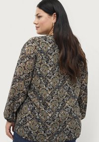 Zwarte blouse met een paisley patroon in goud, groen en blauw. Lange mouwen met elastische manchetten en een losvallend ontwerp.