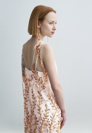 Egy ujjatlan ruha puha rózsaszín anyagból, arany leveles hímzéssel és átlátszó oldalakkal, hosszú lógó fülbevalók díszítéssel.