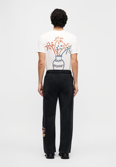 Άσπρο κοντομάνικο μπλουζάκι με πολύχρωμο γραφικό βάζο στην πλάτη· συνδυασμένο με μαύρο παντελόνι άνετης γραμμής με λεπτομερείς διακοσμήσεις.