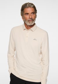 Langarm-Poloshirt in hellbeige, mit einem traditionellen Kragen, einer Dreiknopf-Leiste und einem kleinen, auf der Brust gestickten Logo.