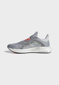 Chaussure de running Adidas grise avec tige en mesh, trois bandes latérales, semelle blanche amortie marquée Stableframe et œillets de lacets rouges.