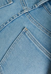 Tela de denim azul claro que muestra bolsillos con costuras contrastantes y detalles de textura visibles, resaltando la construcción de la prenda.