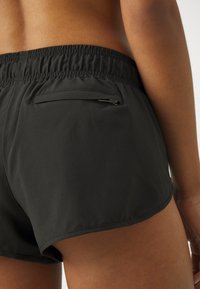 Schwarze Badeshorts mit einem elastischen Bund, einer rückwärtigen Tasche mit Reißverschluss und einer glatten, leichten Stoffoberfläche.