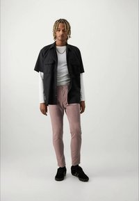 Svart kortärmad skjorta över en vit långärmad tröja, kombinerad med ljusrosa byxor och svarta sneakers. Avslappnad, figurnära silhuett.