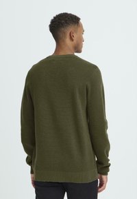 Maglione a girocollo di colore verde scuro, realizzato in maglia, con maniche e fondo a coste, tessuto strutturato e vestibilità comoda. Cuciture dettagliate visibili.