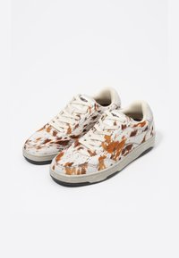 Białe sneakersy z brązowym wzorem w kropki, wykonane z teksturowanego materiału, z gumową podeszwą i płaskimi sznurowadłami. Akcentowane beżowym wykończeniem.