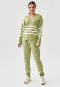 Lichtgroene gebreide trui met witte horizontale strepen, V-halsontwerp, gecombineerd met bijpassende groene broek en beige sneakers.