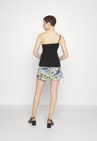 Top preto sem mangas com uma alça, combinado com calções coloridos e estampados com desenhos de flores e pássaros. Sandálias pretas de salto bloco.