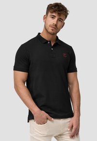 Sort polo-shirt lavet af et glat stof, med en to-knaps placket, korte ærmer og et lille rødt logo på brystet.