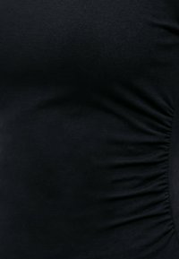 Κοντινή λήψη μαύρου υφάσματος με συγκεντρωμένες ραβδώσεις στη δεξιά πλευρά, που δείχνει την υφή και την ελαστικότητα του υλικού.