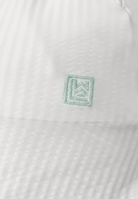 Vit keps med texturerad tyg, med en broderad mintgrön logotyp i form av en kvadrat, placerad på frontpanelen.