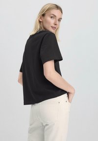 Schwarzes T-Shirt mit kurzen Ärmeln und lockerem Schnitt, mit rundem Halsausschnitt und glattem Baumwollstoff, kombiniert mit hellen Jeans.