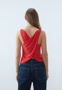 Top in satin rosso con design retro drappeggiato e spalline incrociate, abbinato a jeans in denim blu scuro a vita alta con tasche posteriori.