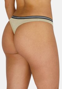 Beige Strings mit einem elastischen, schwarz gestreiften Bund, aus Baumwollstoff, minimaler Bedeckung und glatter Textur.