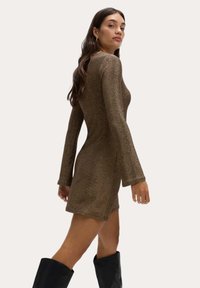 Braunes glitzerndes Minikleid mit langen Ärmeln, figurbetontem Silhouette, strukturiertem Material, rundem Ausschnitt und kombiniert mit knielangen schwarzen Stiefeln.