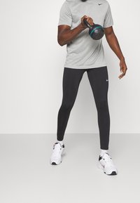 Szara sportowa koszulka z krótkim rękawem, czarne dopasowane legginsy i białe sneakersy. Legginsy mają małe logo Nike na łydce.