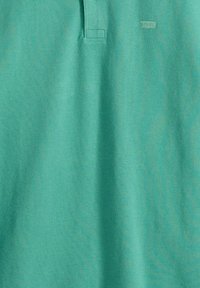 Türkisfarbenes Poloshirt-Stoff mit einer dezenten gewebten Textur und einem kleinen angenähten Etikett nahe dem Kragen.