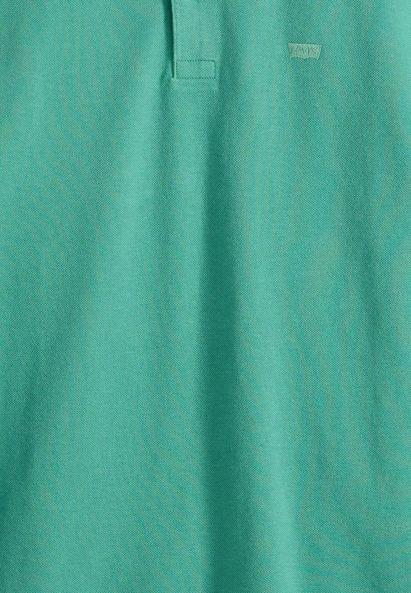 Tela de polo turquesa con una textura tejida sutil y una pequeña etiqueta cosida cerca del cuello.