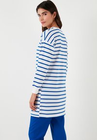 Túnica de manga larga en rayas blancas y azules, con puños de canalé y aberturas laterales para mayor comodidad. Corte casual y textura suave.