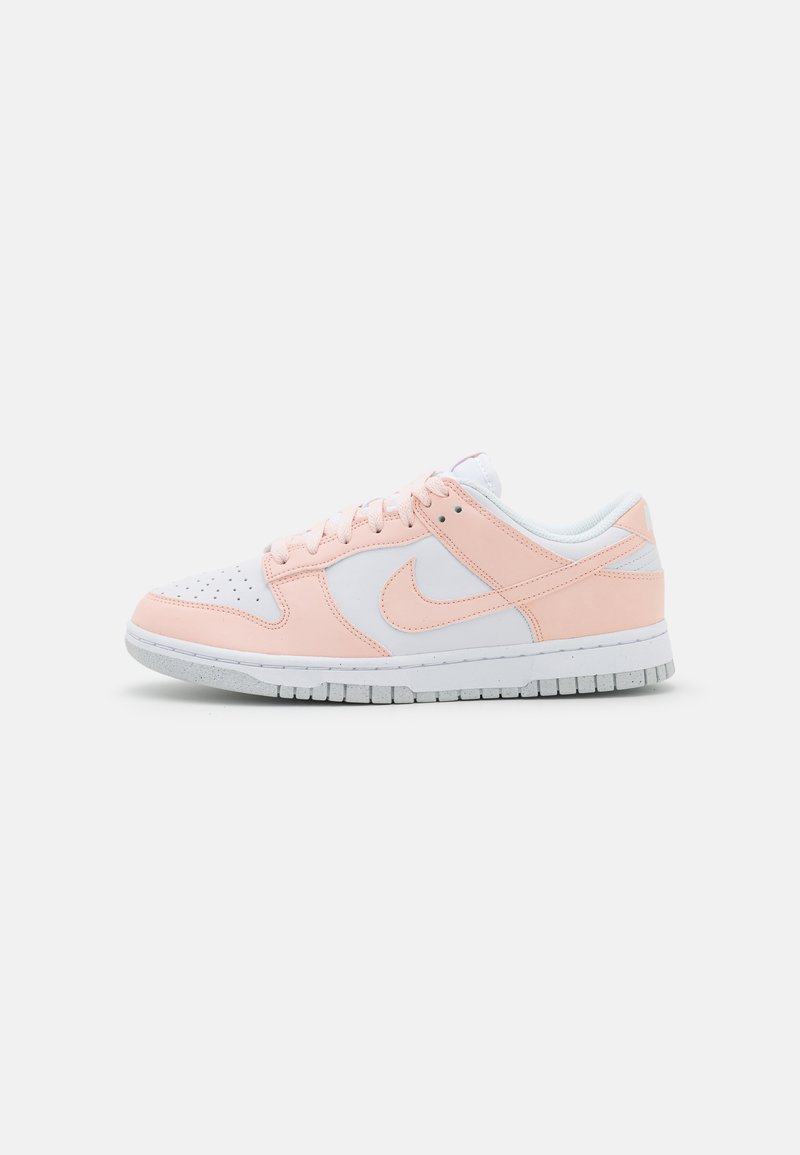 Nike-Sneaker mit einem weißen Lederoberteil und hellrosa Akzenten, einem gepolsterten Kragen und einer strukturierten Gummisohle, Seitenansicht.